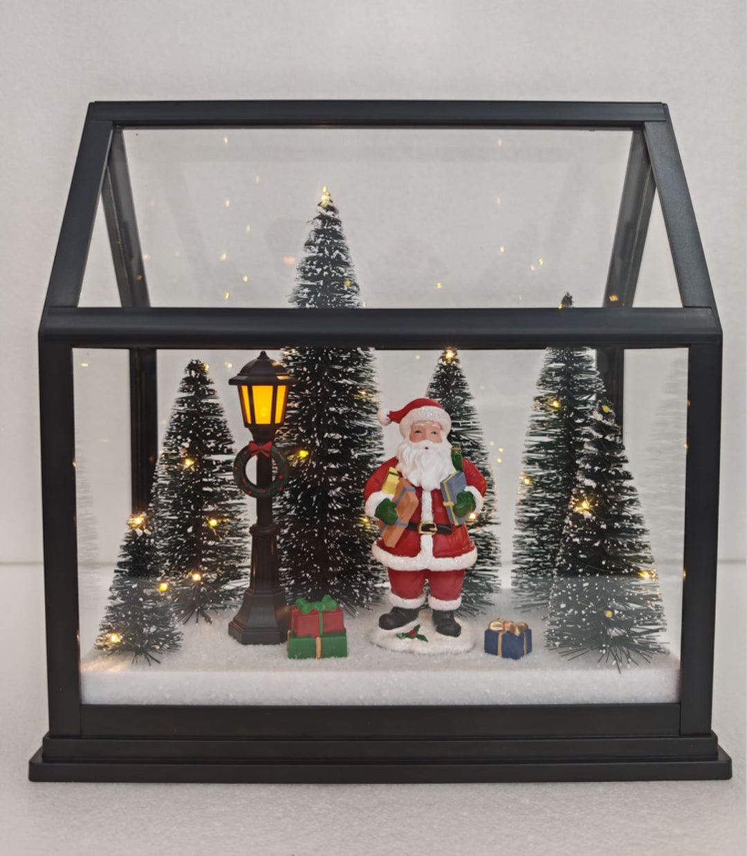 A glass Christmas light up lantern with trees, Santa, gifts &amp; lamp post. 