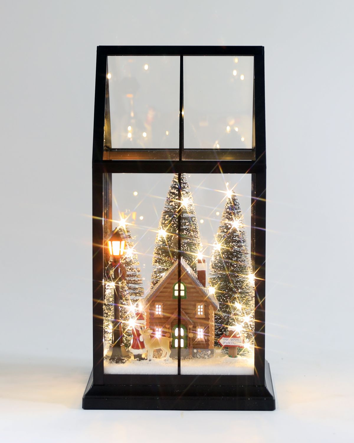 Decorative glass lantern with miniature house, trees, and lights on a white background