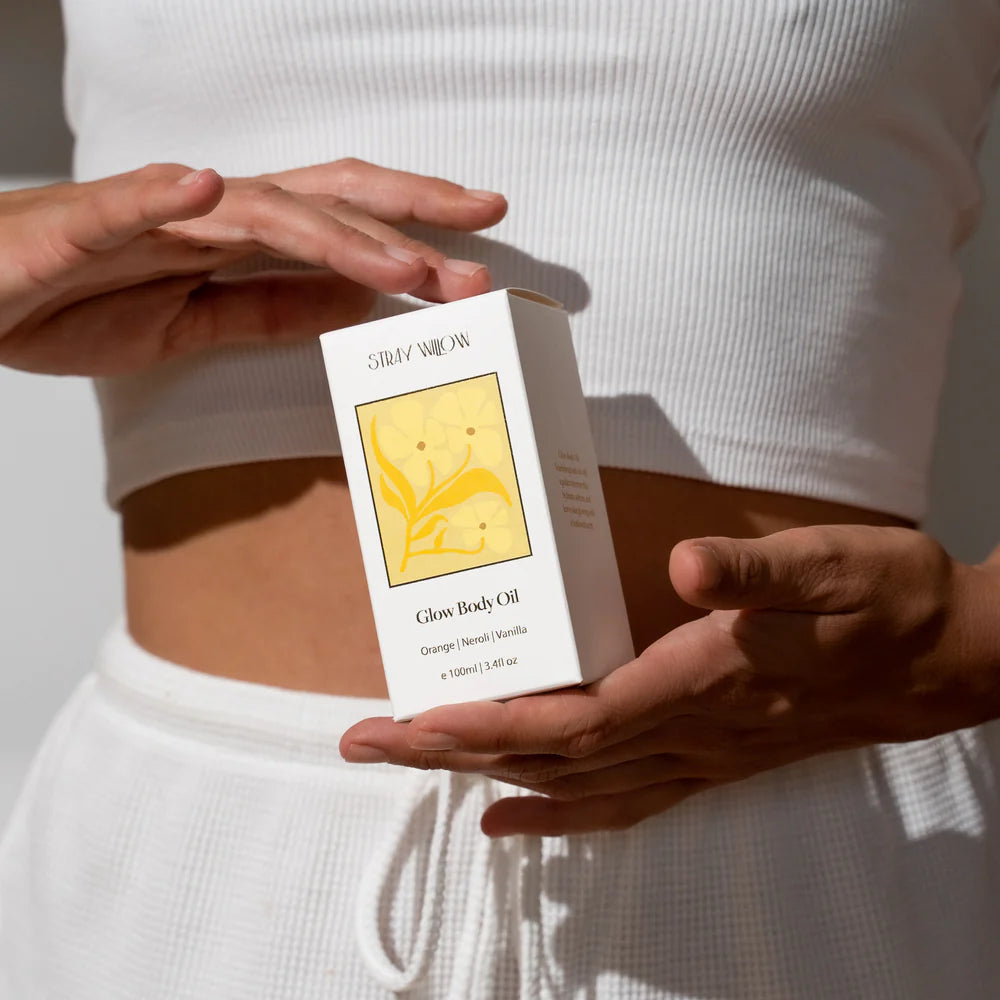 Person holding a box of Glow Body Oil with a white background