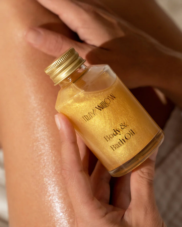 Small bottle of body and bath oil held by a hand with a blurred background