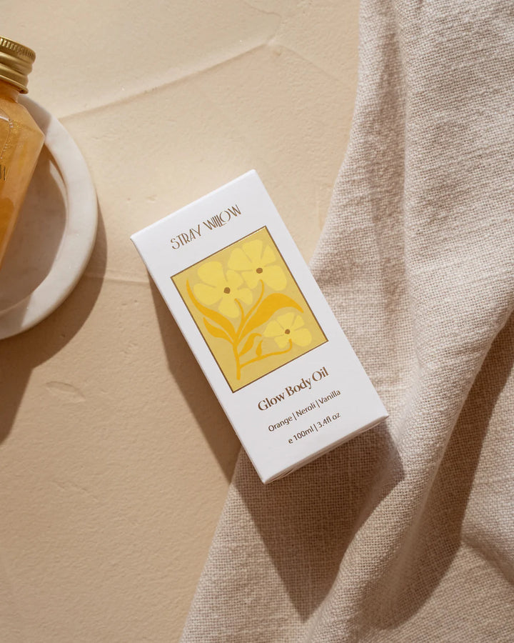 Stray Willow Glow Body Oil packaging on a beige surface with a towel