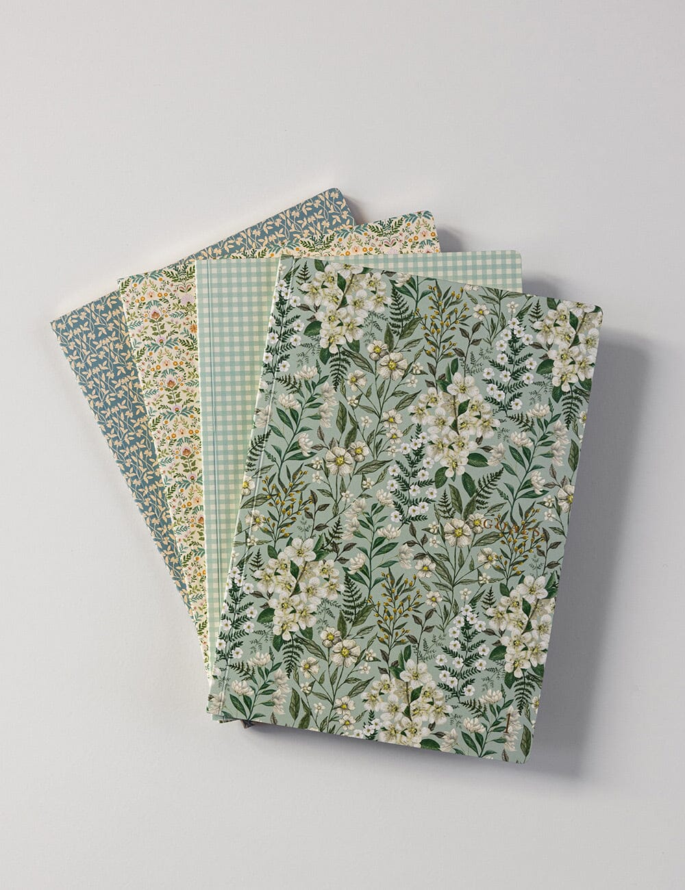 Set of four notebooks with floral and checkered patterns on a light gray background