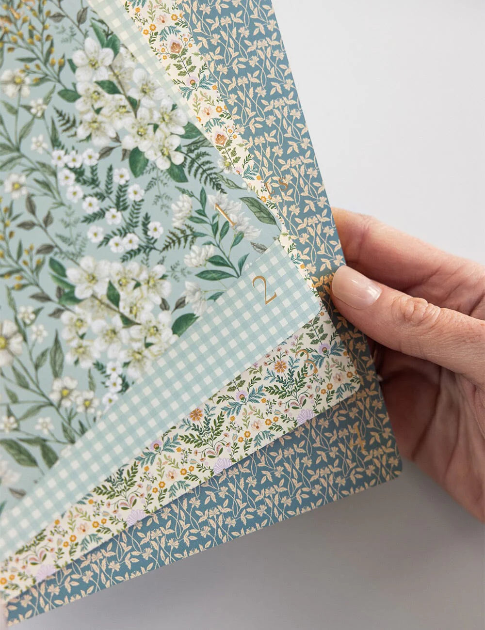 Hand holding a stack of floral and checkered patterned paper sheets.