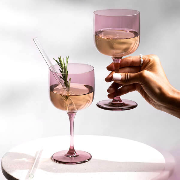 Two pink wine glasses with a hand holding one, on a white background