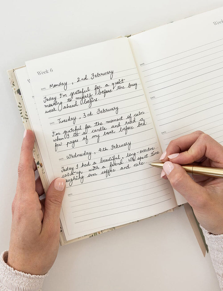 Person writing in a notebook with a gold pen on a white surface
