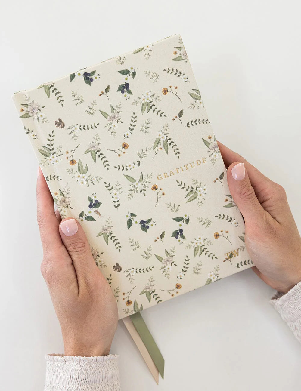 Hand holding a notebook with floral pattern on a white background