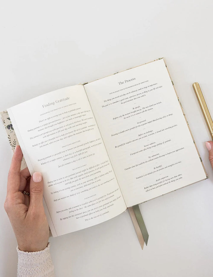 Open book with text on a white surface, held by hands.