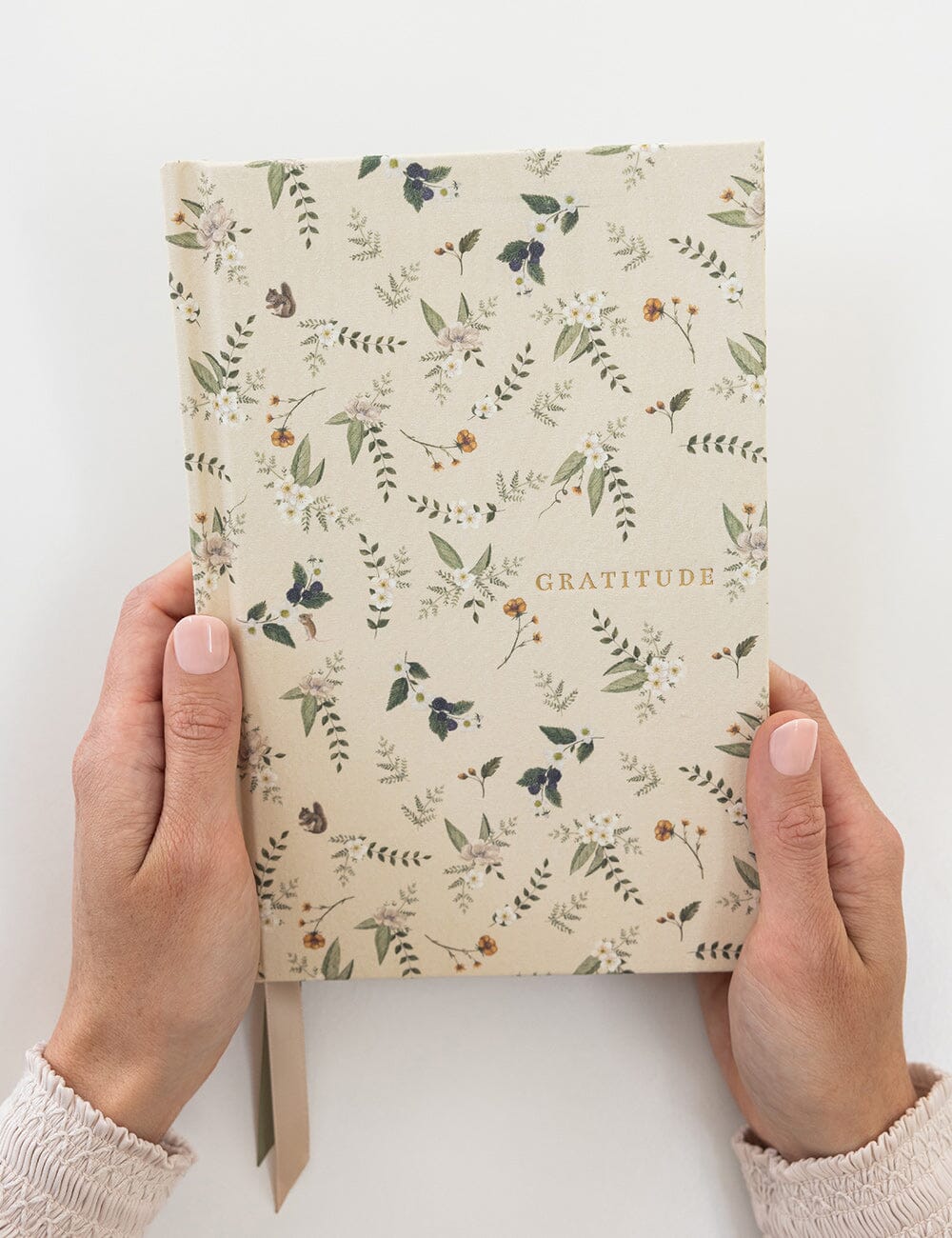 Notebook titled 'Gratitude' with floral design held by hands on a white background