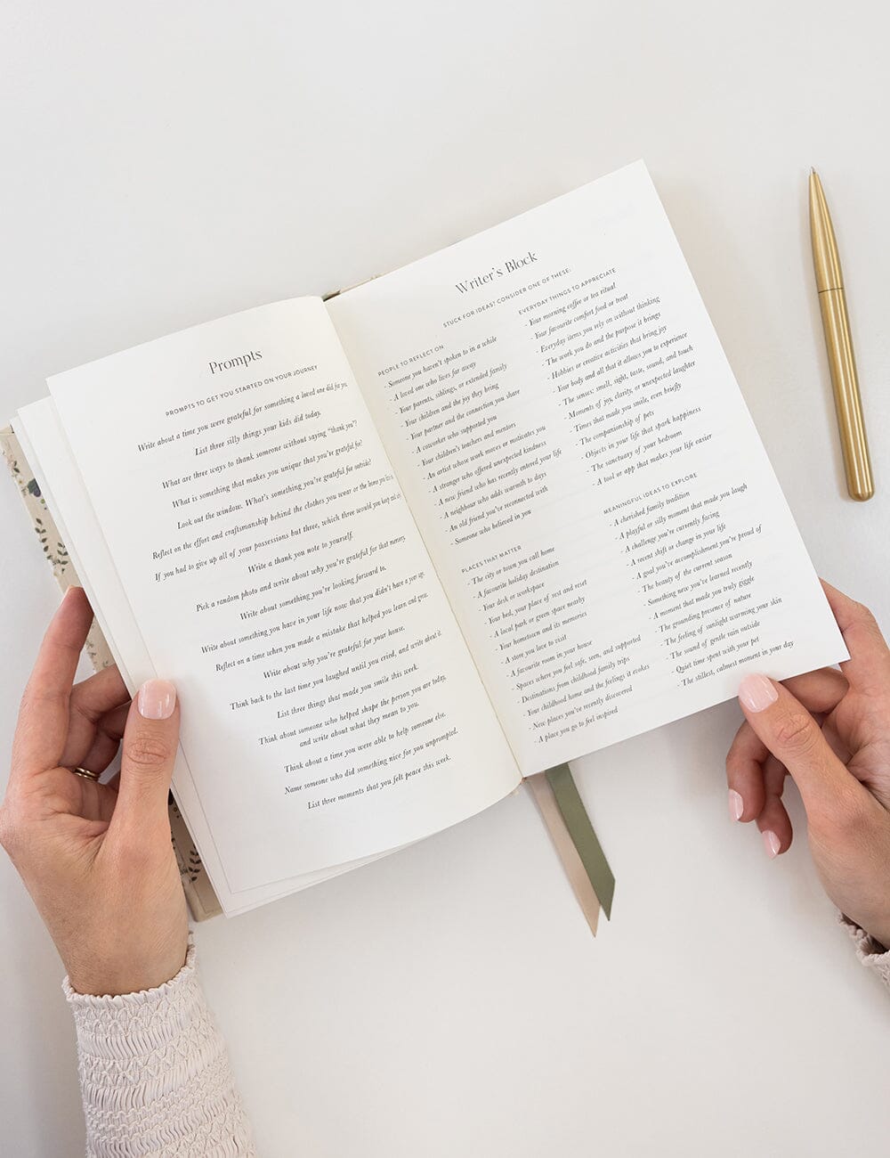 Open book held by hands on a white surface with a pen next to it