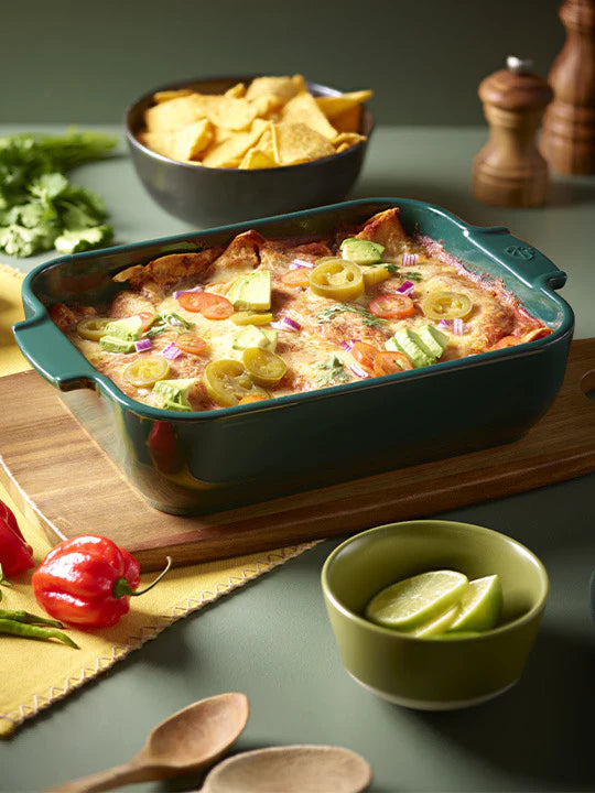 Baked dish with vegetables in a green baking dish on a wooden cutting board, surrounded by ingredients.