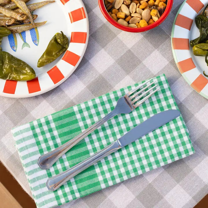Green checkered napkin with silverware on a table with food plates and snacks.