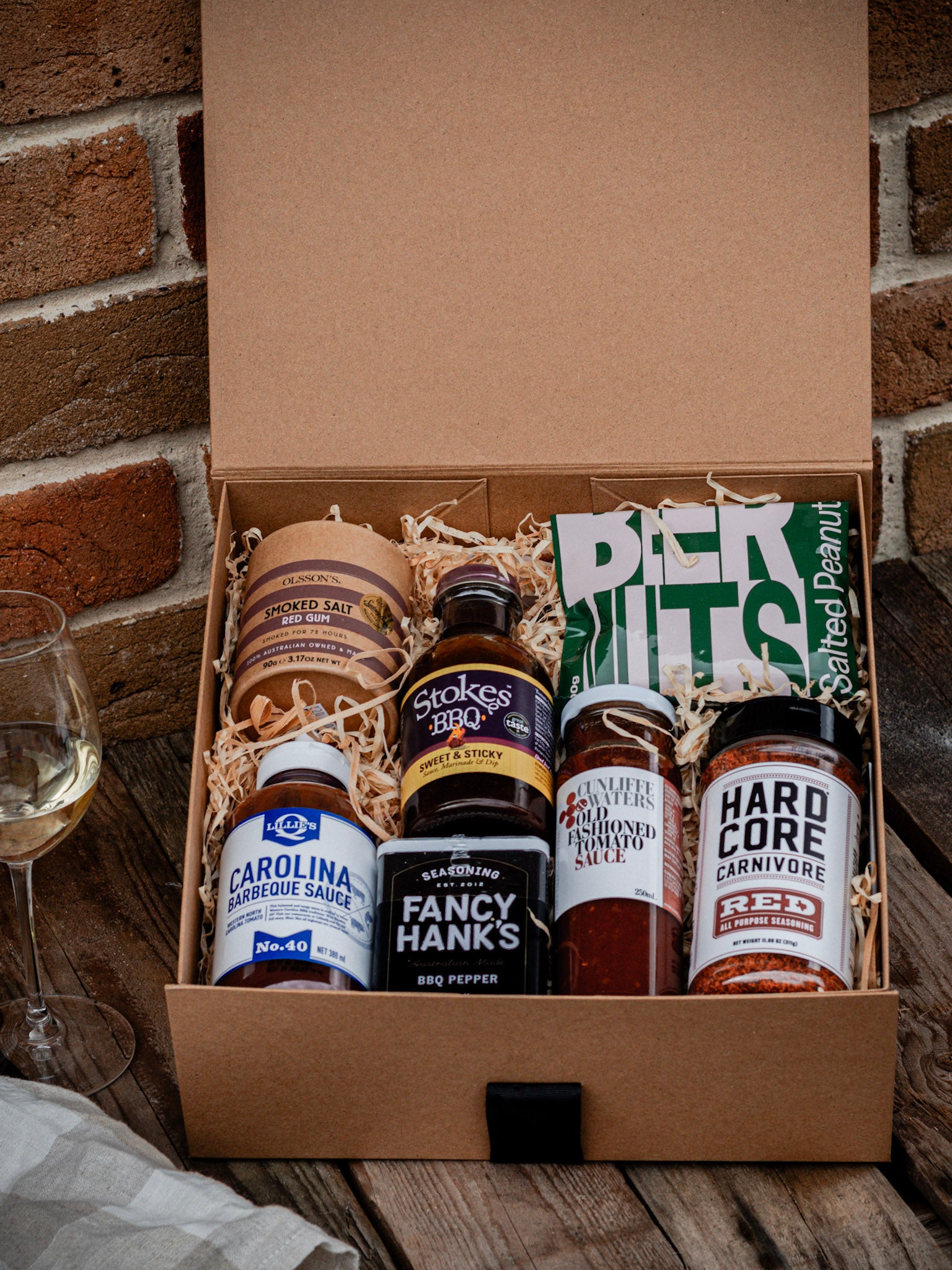 Box of barbecue sauces and a bag of peanuts on a wooden surface with a brick wall background