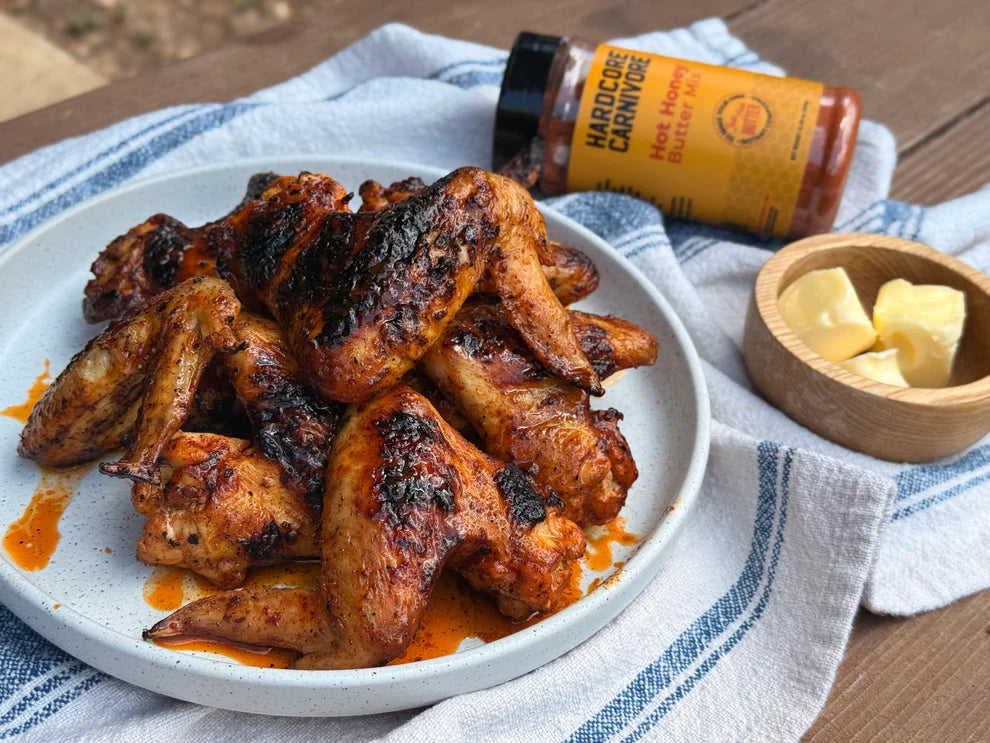 Plated chicken wings with a bottle of hot sauce and butter on a wooden surface