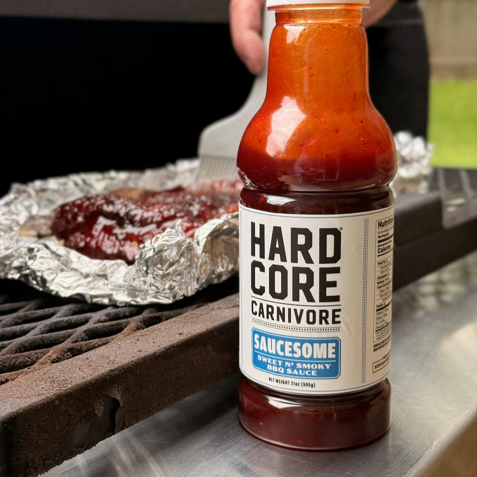 Bottle of Hardcore Carnivore Saucesome sauce on a grill with ribs in the background
