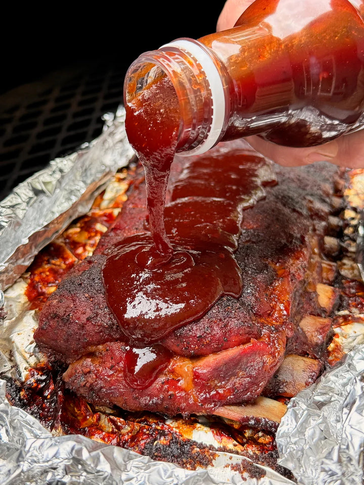Barbecue sauce being poured over ribs on tinfoil