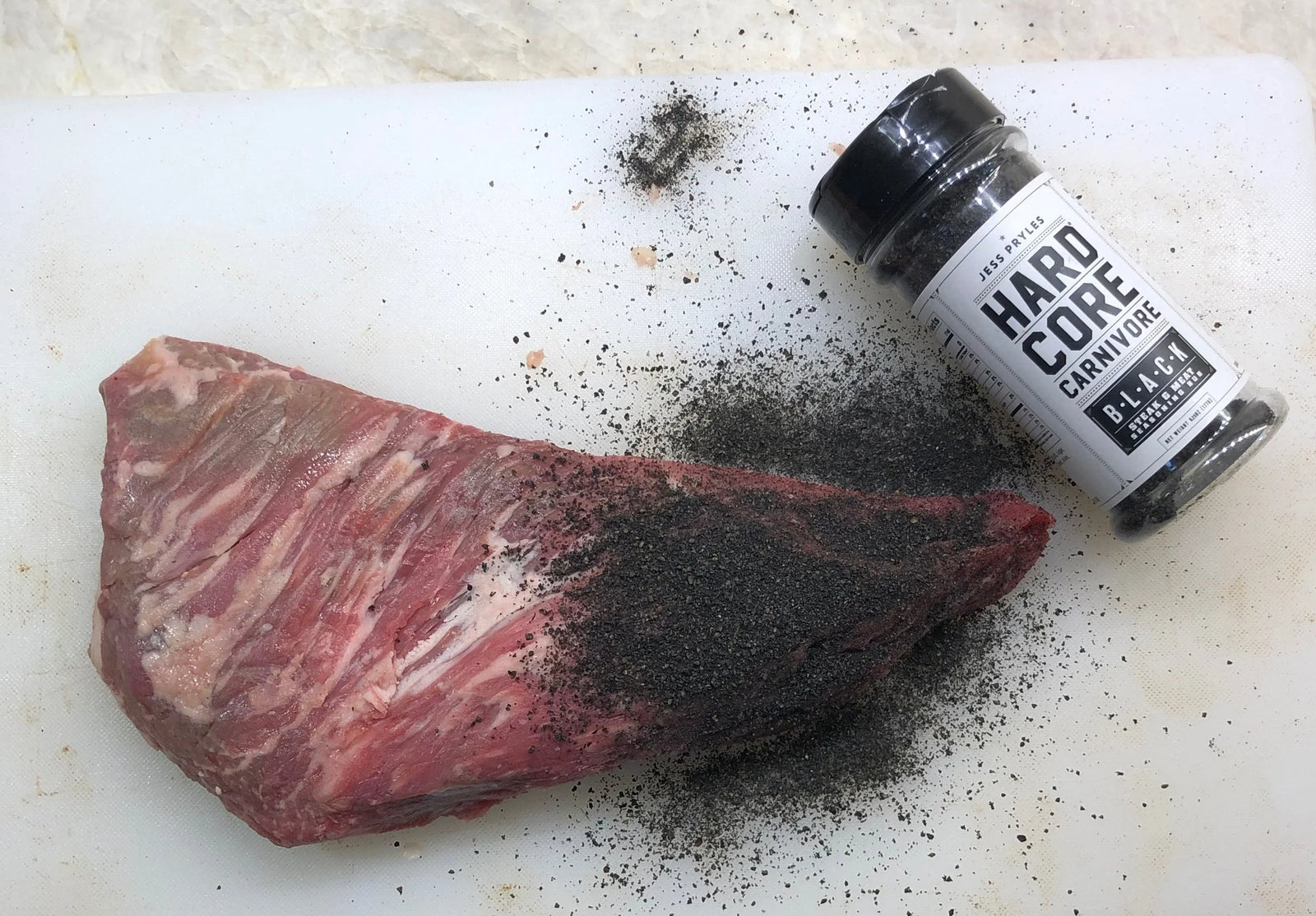 Hardcore Carnivore black seasoning with a piece of beef in white chopping board