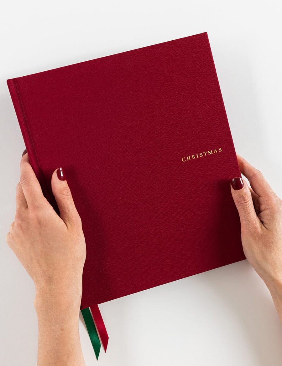 Red book titled 'Christmas' held by hands on a white background