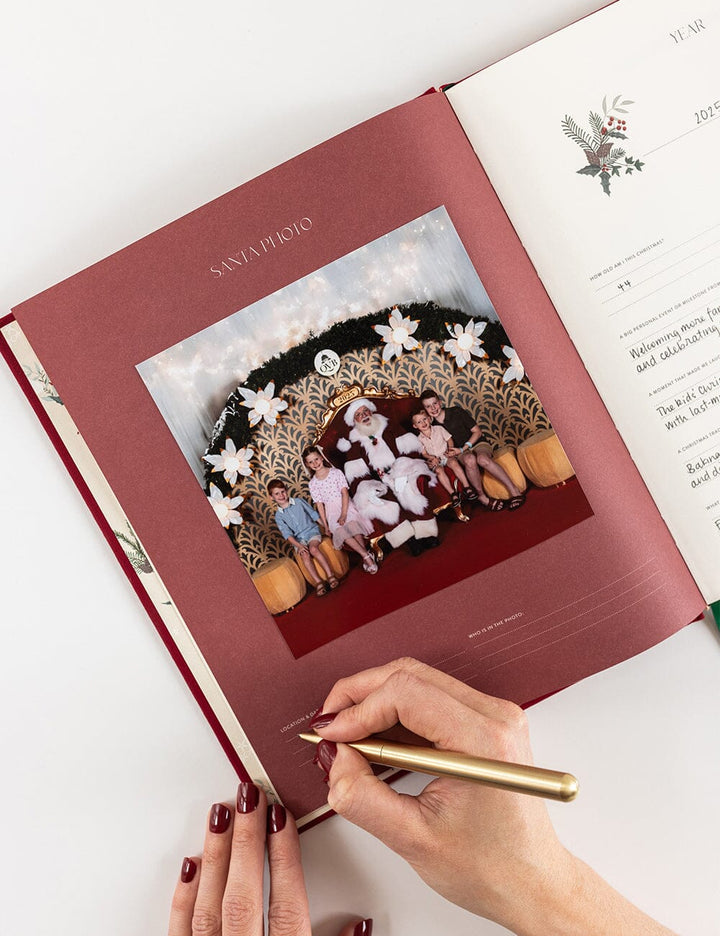 Person signing a red album with a gold pen on a white surface