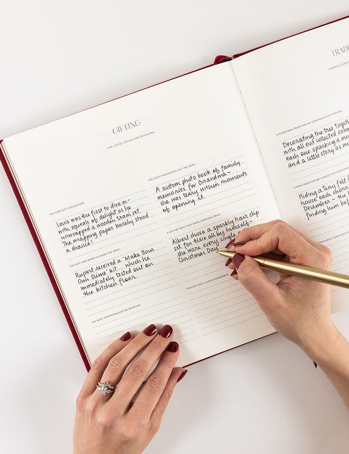 Person writing in a journal with a gold pen on a white surface