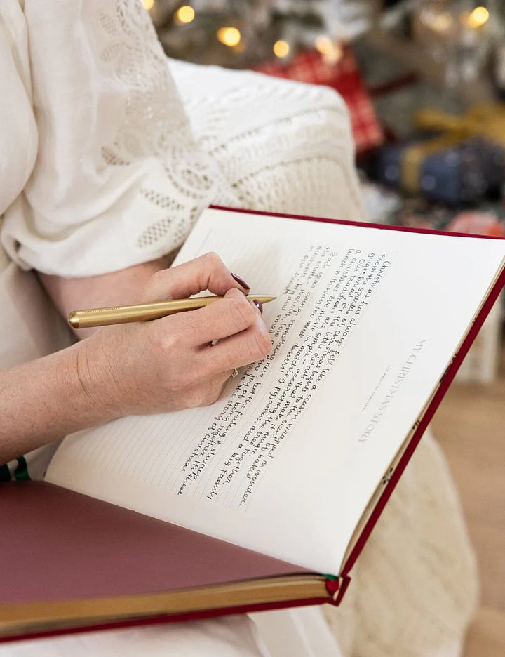 Person writing in a red notebook with a blurred festive background