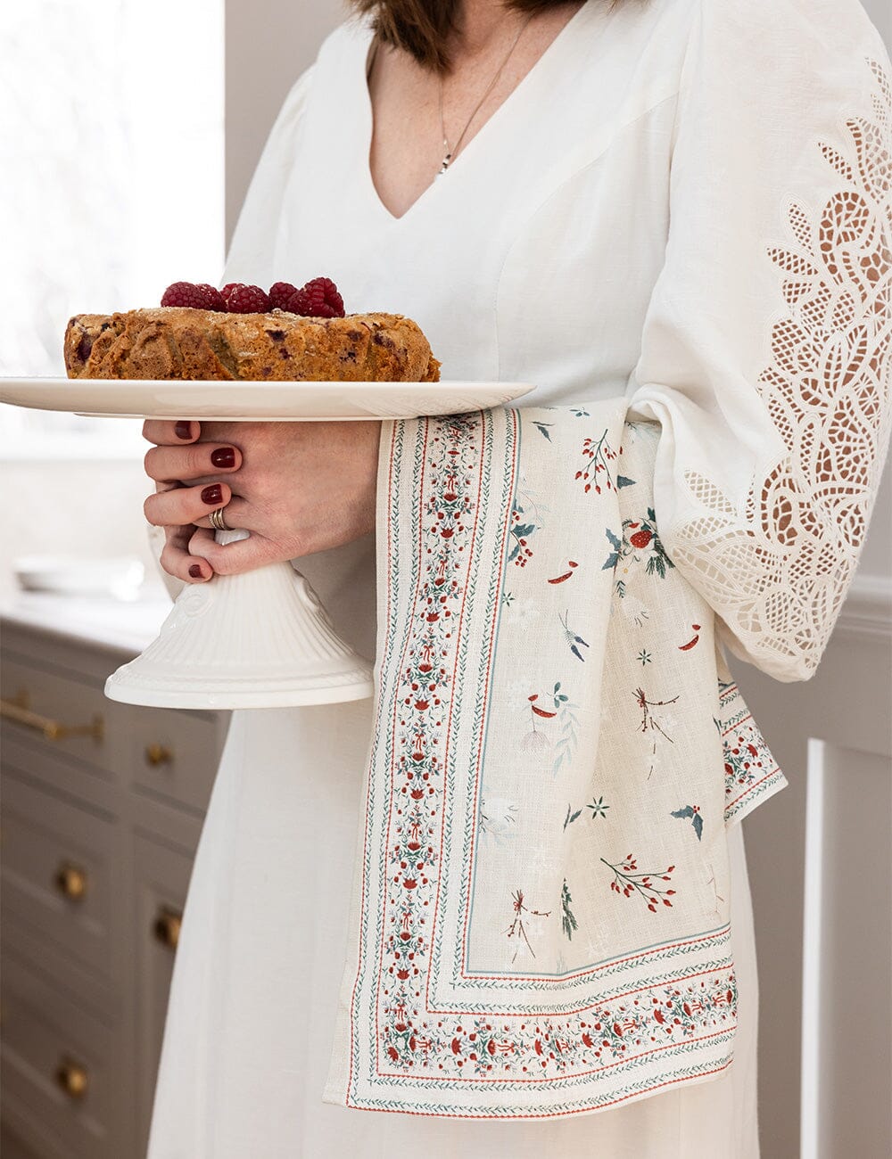 A christmas tea towel over someones arm who is holding a cake stand