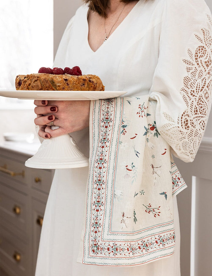 A christmas tea towel over someones arm who is holding a cake stand