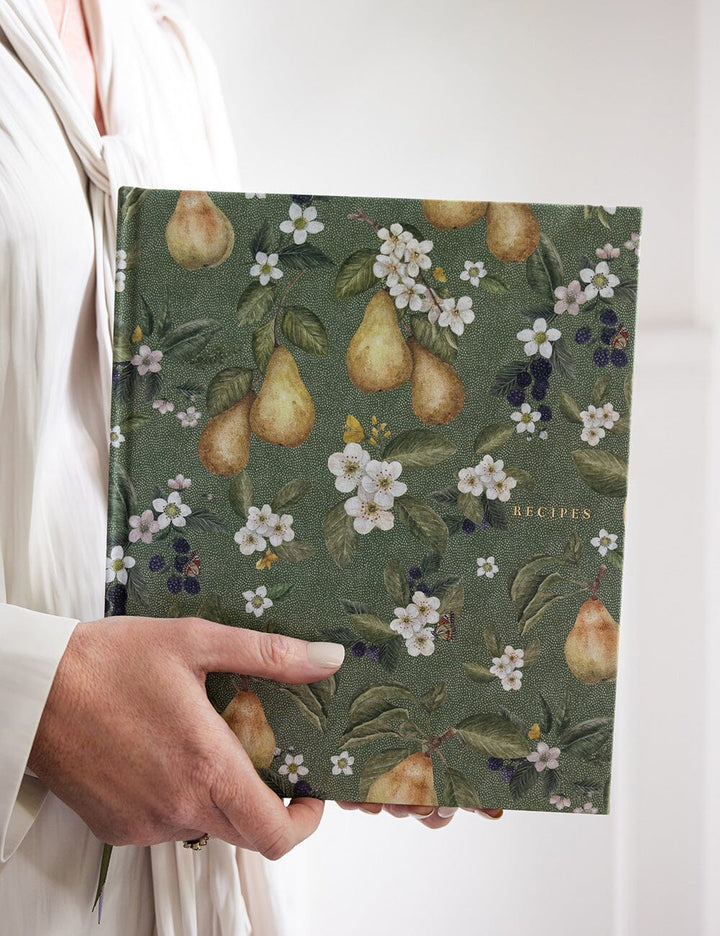 Hand holding a recipe book with pear and floral pattern