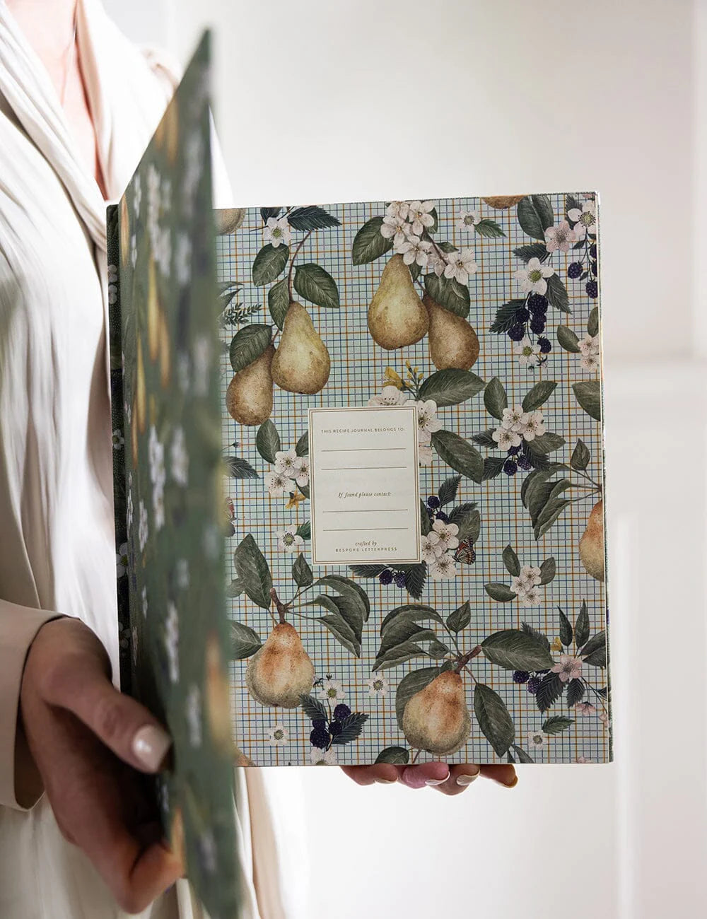 Recipe journal with a floral and fruit design held by a person