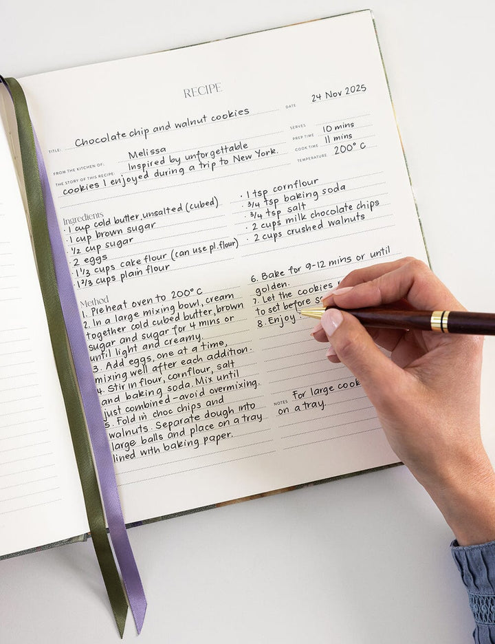 Handwritten recipe for chocolate chip and hazelnut cookies in a notebook with a hand holding a pen.