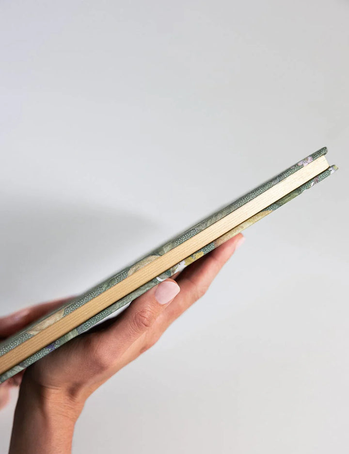 Hand holding a green notebook against a light gray background