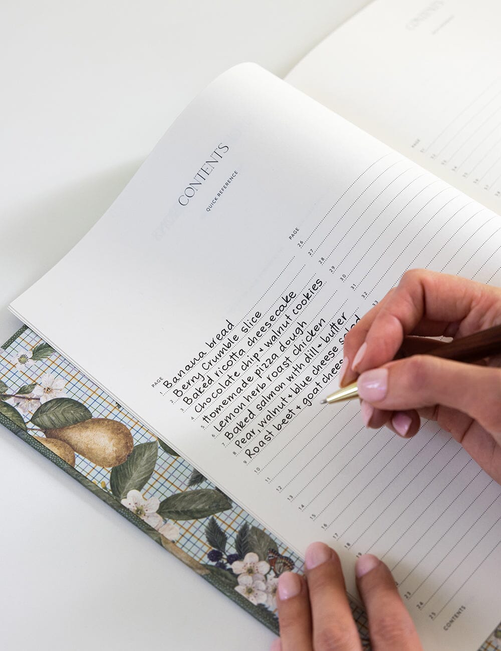 Person writing in a notebook with a decorative pen on a white surface