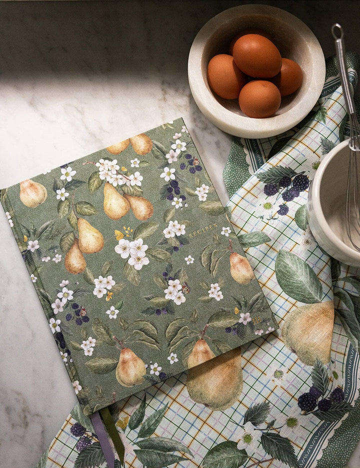 Notebook with floral and fruit design on a kitchen counter with eggs and utensils.