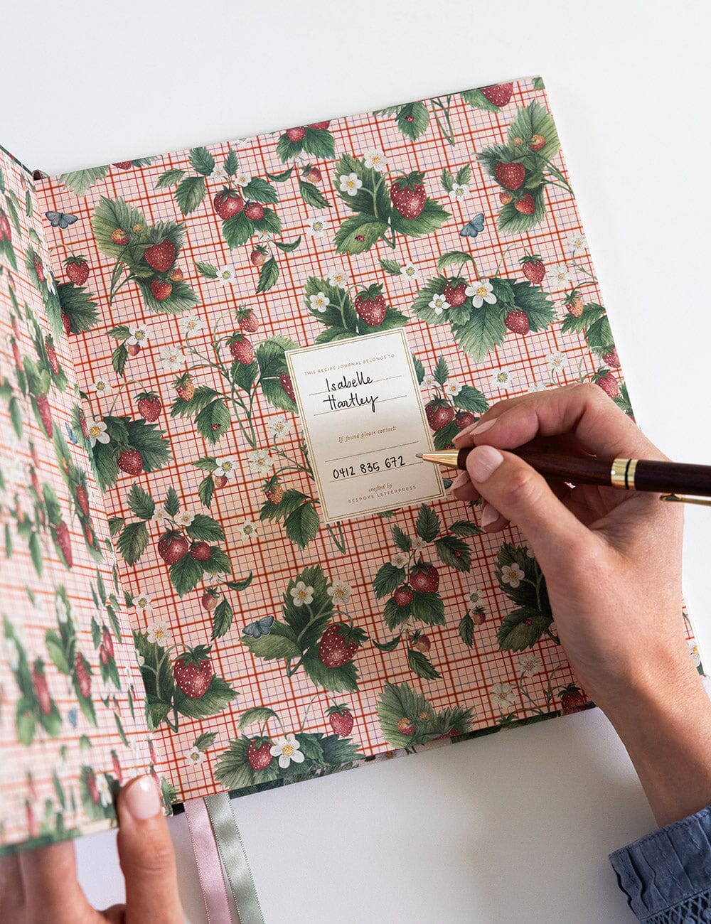 Floral-patterned notebook with a hand holding a pen on a white background