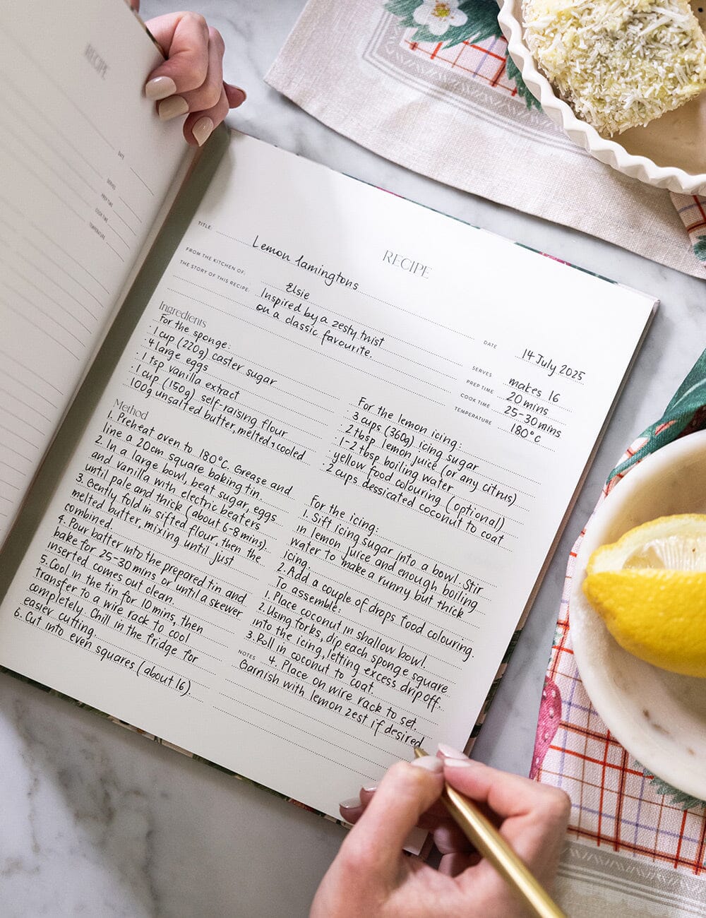 Handwritten recipe in a notebook with lemons and baking ingredients on a marble surface