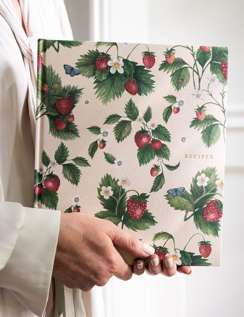 Hand holding a recipe book with strawberry and leaf pattern