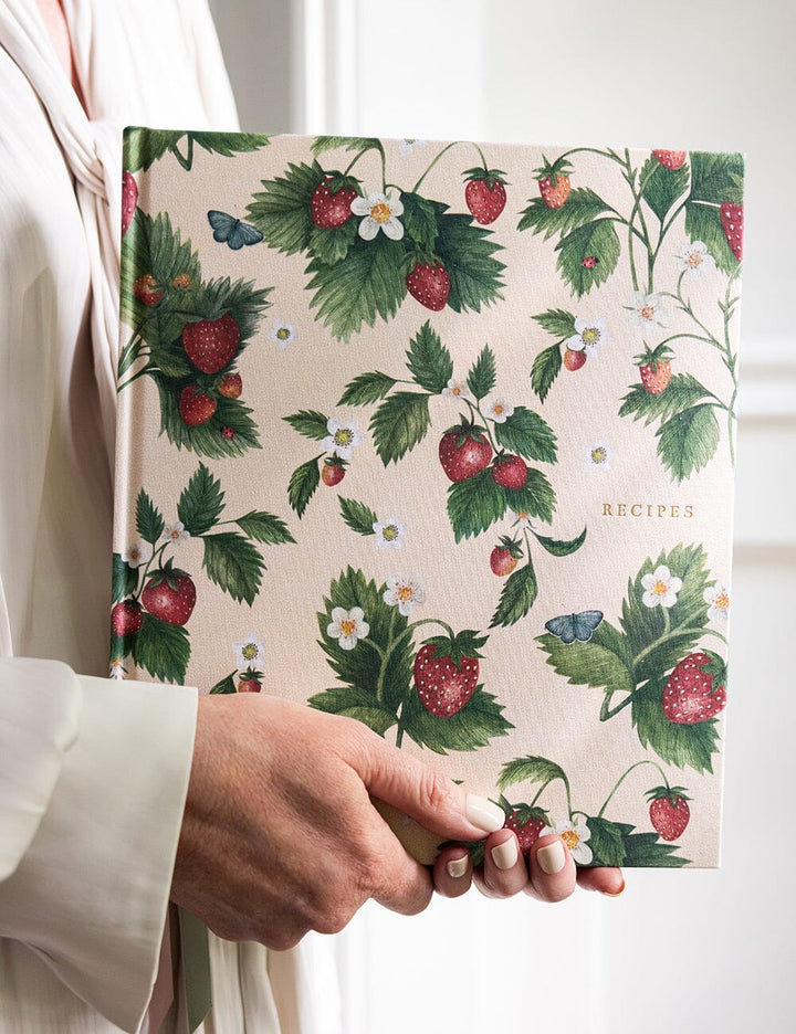 Hand holding a recipe book with strawberry and leaf pattern