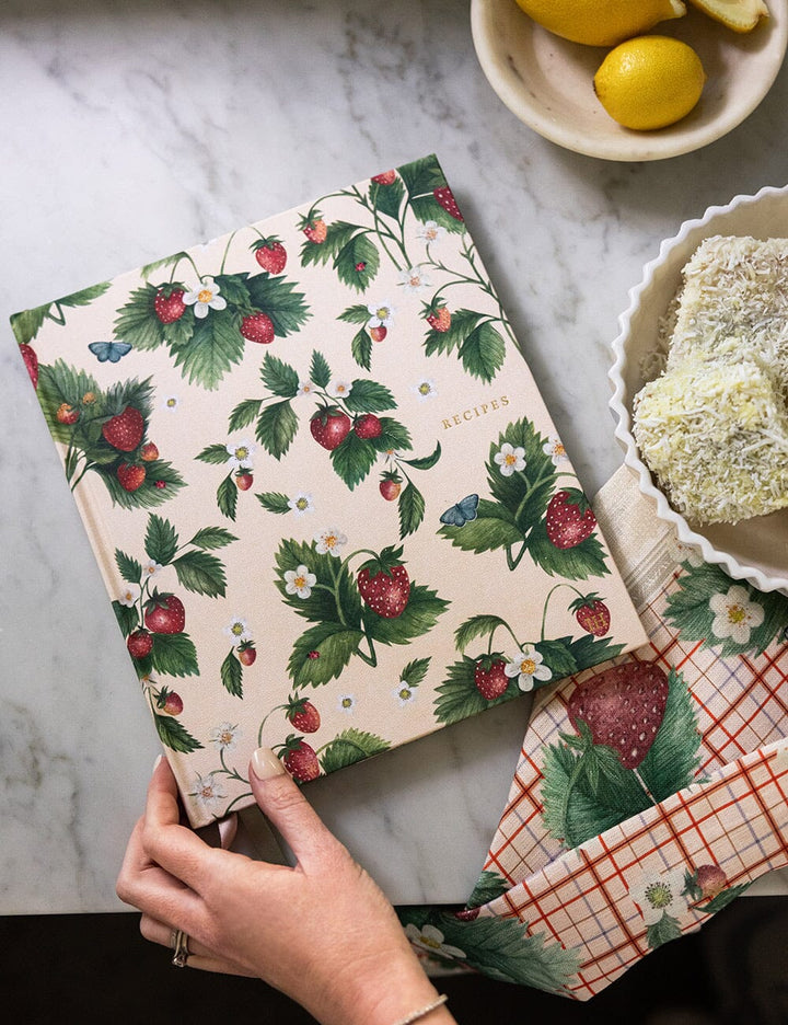 Floral-patterned book held by a hand on a marble surface with lemons and a bowl of cereal in the background.