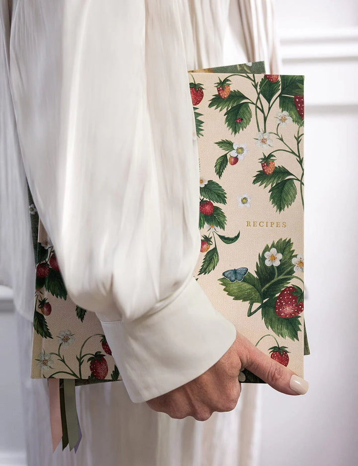 Hand holding a recipe book with floral and strawberry design