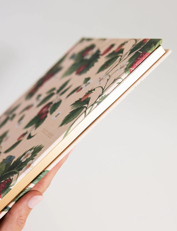 Hand holding a notebook with floral pattern on a light background