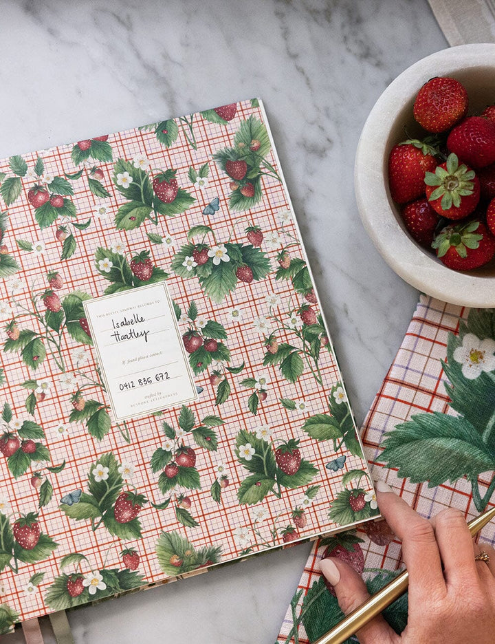Notebook with strawberry pattern on a marble surface with a bowl of strawberries.