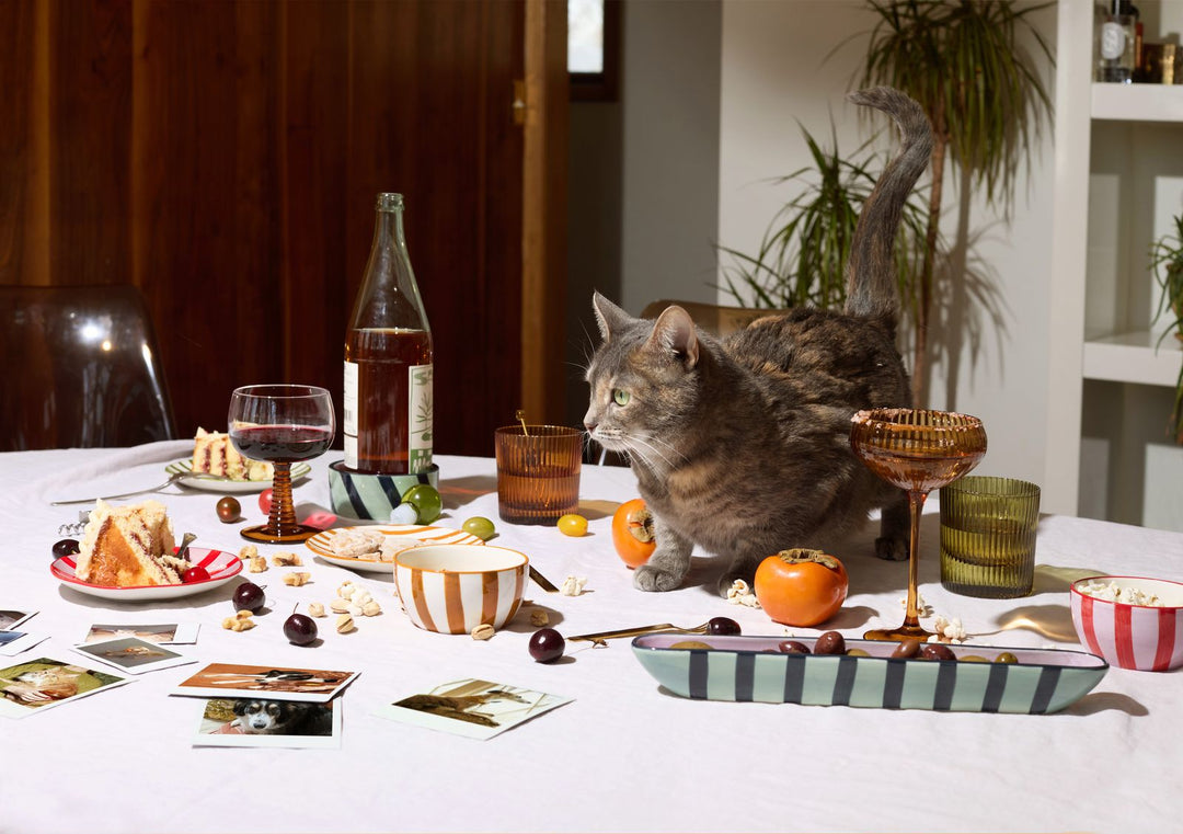 Servingware and glassware on a table wit a white tablecloth with a cat on it