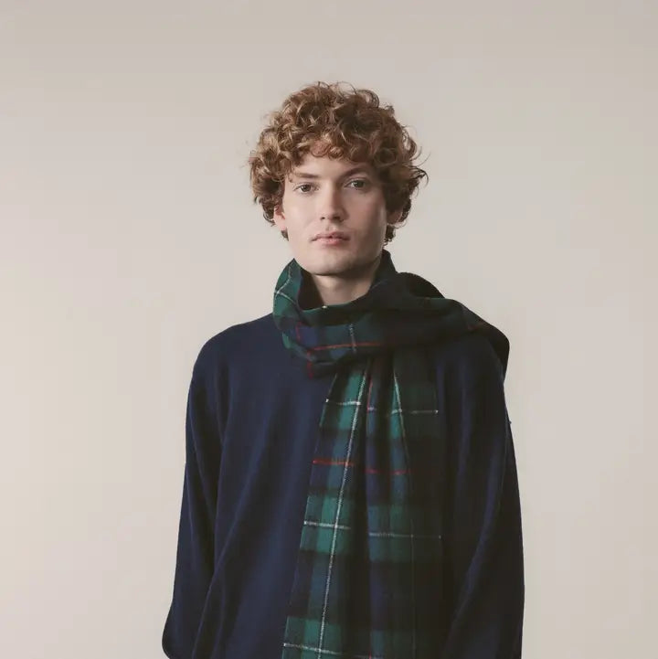 Person wearing a dark blue sweater and a green plaid scarf against a plain background