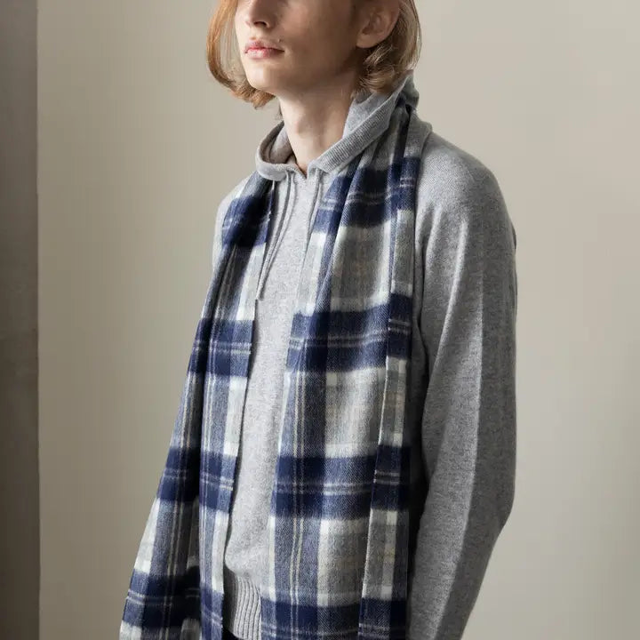 Person wearing a gray hoodie and blue plaid scarf against a plain background