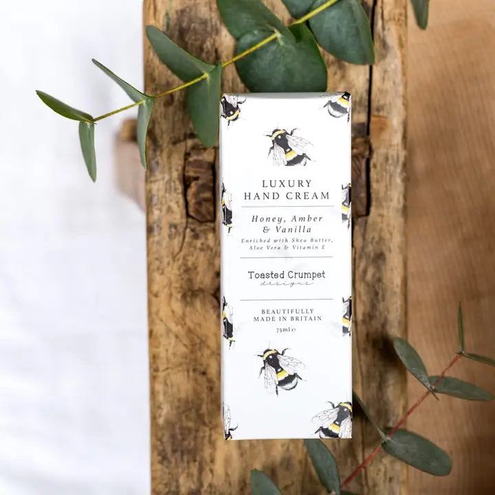 Luxury hand cream in a gift box with a decorative label on a wooden board with green leaves.