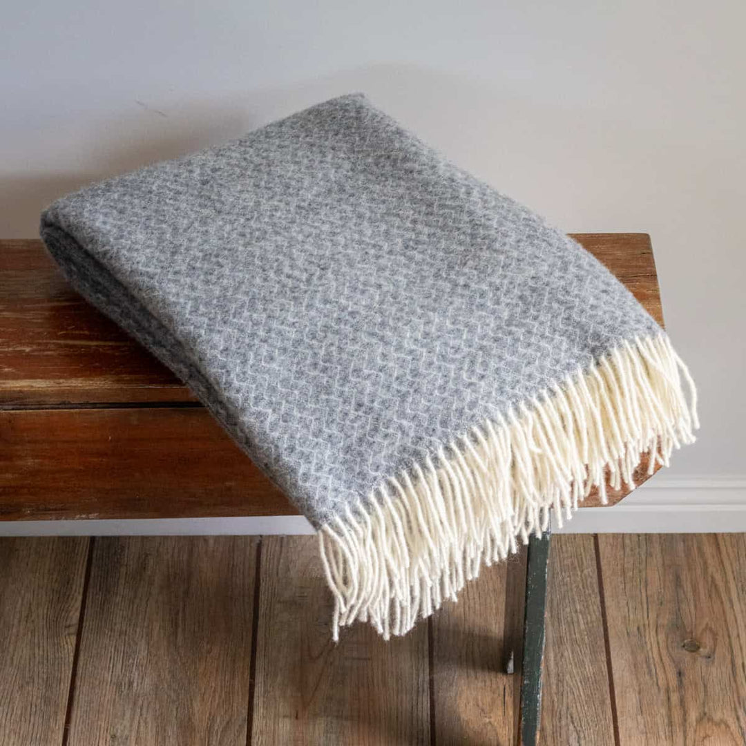 Gray blanket with white fringe draped over a wooden bench.