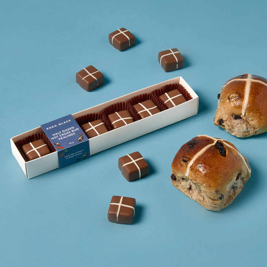 Box of hot cross buns praline chocolates next to baked hot cross buns with a blue label on a blue background