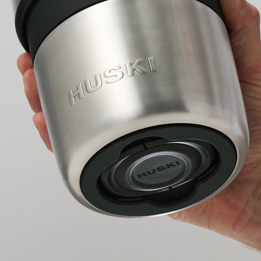 Silver and black Huski champagne cooler held in a hand against a light gray background
