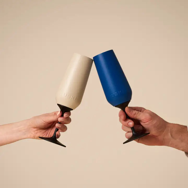 Two hands holding a beige and blue champagne glass against a beige background