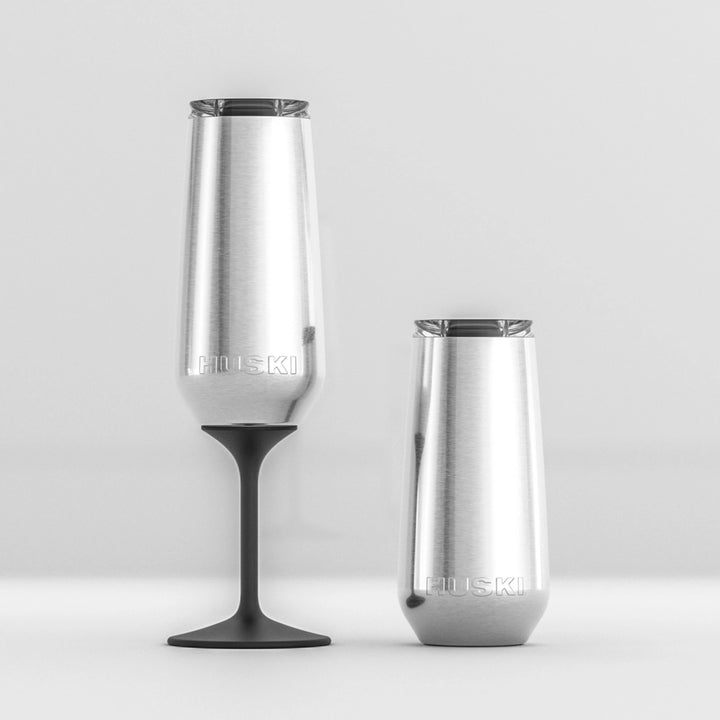 Two stainless steel huski champagne tumblers with black stems on a light gray background