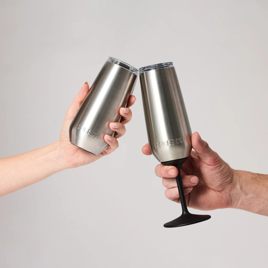 Two hands holding stainless steel champagne glasses against a plain background